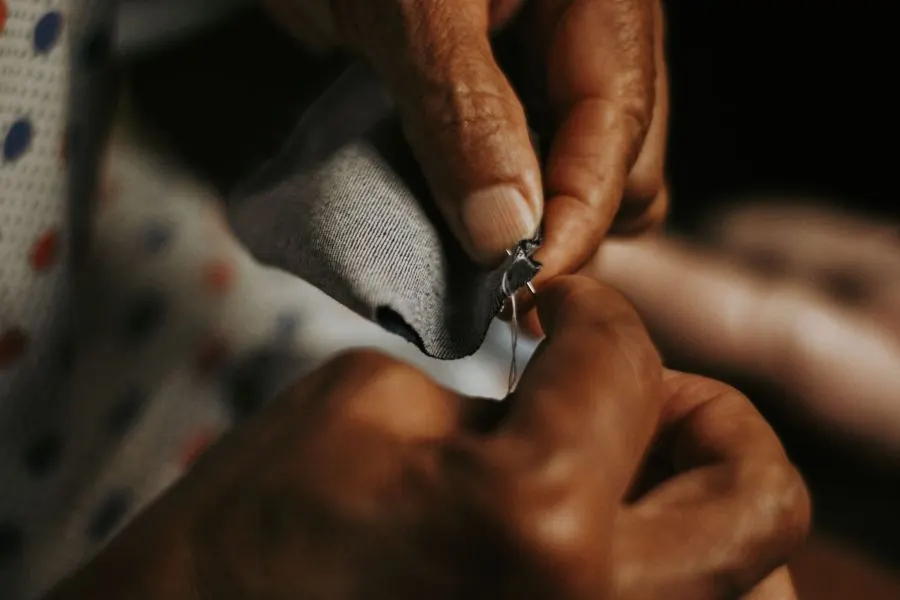 Close-up of adult hands sewing gray fabric thread and needle, showcasing craftsmanship.