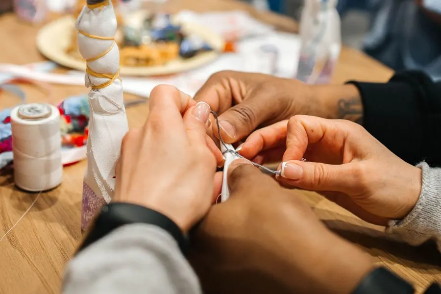 Hands sewing with a needle and thread in a close-up view on a wooden table.