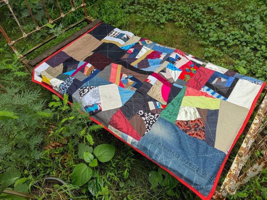 Colorful patchwork quilt on a rustic bed frame amidst lush greenery, ideal for cozy outdoor scenes.