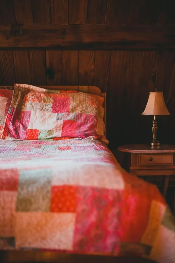 Warm rustic bedroom interior featuring a colorful patchwork quilt and wooden bedside table.